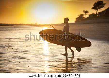 silhouette of a man with his paddle board on the beach at sunset
