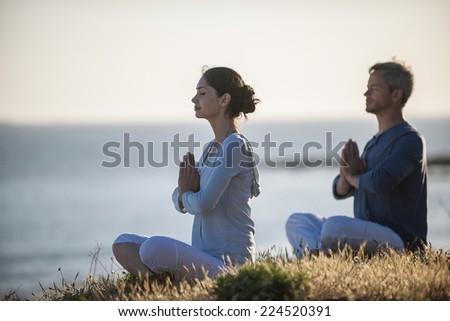 handsome couple practicing meditation exercises on the beach at sunset