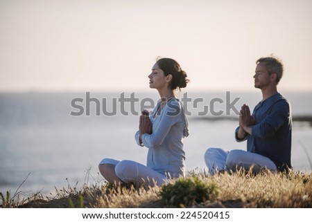 handsome couple practicing meditation exercises on the beach at sunset