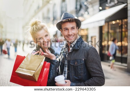 a trendy young couple walks in the city at christmastime, the young woman wears a leather jacket , shopping bags at her arm and the man a cup of coffee in hand