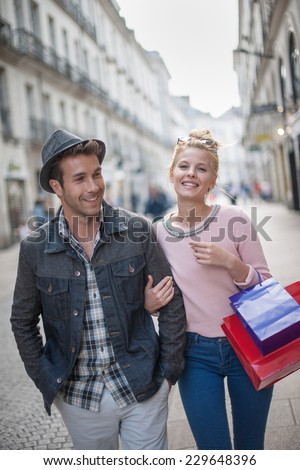 a trendy young couple walks in the city, the young woman has shopping bags at her arm