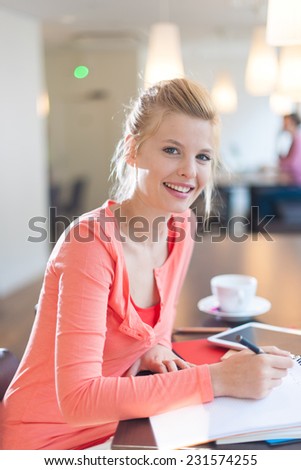 smiling young student installed in a cafe to work, writing on a pad of paper
