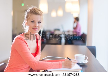 smiling young student installed in a cafe to work, writing on a pad of paper