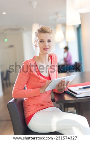 smiling young female student sitting in a cafe to work, using a digital tablet