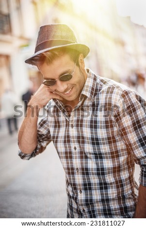 portrait of a trendy young man walking in the street, he wears a hat and sunglasses
