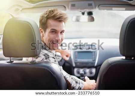 handsome man looking at camera sitting in a car, view from rear seat