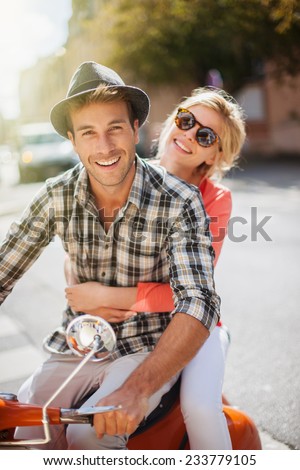 glamorous  young couple riding  a vintage scooter in the street, man wears a hat and woman has a topknot and sunglasses