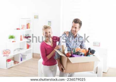 portrait of an handsome couple moving in  a new apartment and carrying a box with various objects