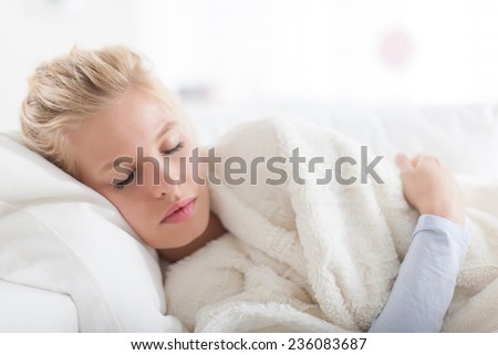 Beautiful blond woman lying on a couch wrapped in a white blanket