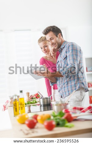 Handsome couple looking for a recipe on a digital tablet for cooking at home, vegetables on the work plan