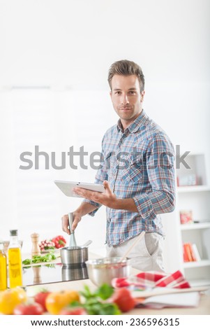 Handsome man looking for a recipe on a digital tablet for cooking at home, vegetables on the work plan at foreground