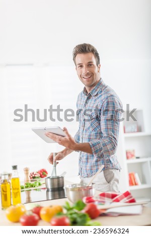 Handsome man looking for a recipe on a digital tablet for cooking at home, vegetables on the work plan at foreground