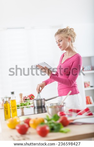 Cheerful young woman looking for a recipe on a digital tablet for cooking at home, vegetables on the work plan at foreground