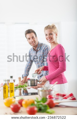 Handsome couple cooking on a cook-top at home, vegetables on the work plan