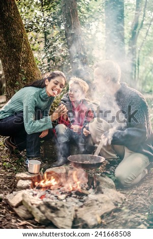 in the evening, cheerful family roasting marshmallows in the woods on a campfire