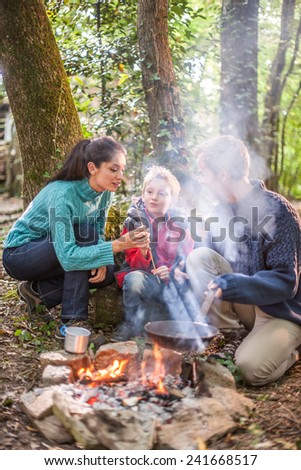 in the evening, cheerful family roasting marshmallows in the woods on a campfire