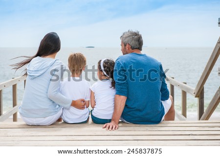 family back sitting on a wood pontoon at seaside watching the horizon