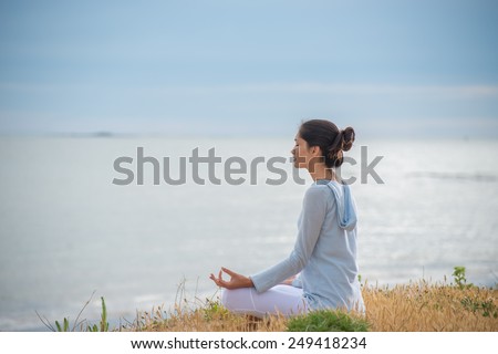 An attractive woman is sitting face to the ocean in lotus position.