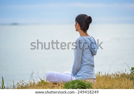 An attractive woman is sitting face to the ocean in lotus position.