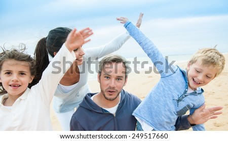smiling parents and their two children, a beautiful family is posing with their arms up like planes at the beach.