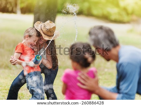 cheerful family having fun she does a water gun fight, mom and son against dad and daughter, focus on mom and her son