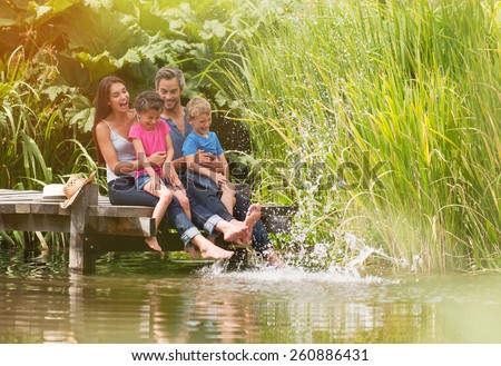 summertime, portrait of an happy family sitting on the edge of a wooden pontoon, feet in the river and making splashes
