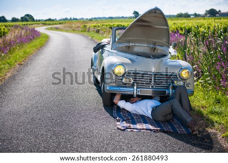 Car problems on a country road. A man in a suit is trying to fix his retro car