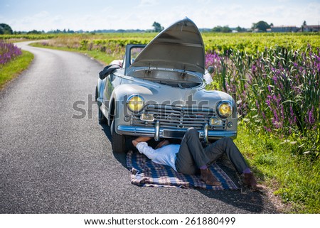 Car problems on a country road. A man in a suit is trying to fix his retro car