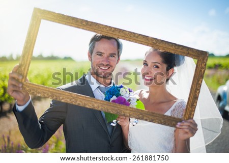 Charming bride and groom posing with a frame for their wedding photos, behind them a lovely country road