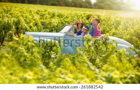 A lovely family is going on vacation in a convertible retro car, they drive on a country road on a sunny day