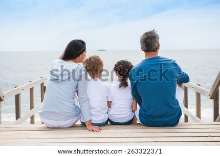 family back sitting on a wood pontoon at seaside watching the horizon