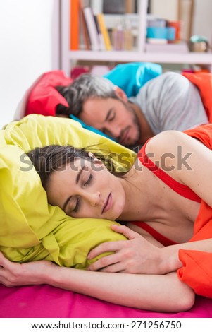 Handsome couple sleeps in bed on bright colored pillows,the woman awakes, bedding is bright color,their sunny apartment is modern and bright