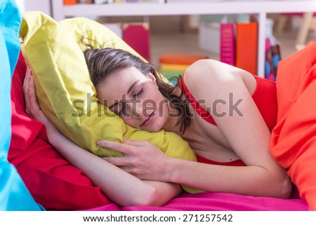 a gorgeous young woman sleeps in bed,  colored pillow in her arms,bedding is bright color, her sunny apartment is modern and bright