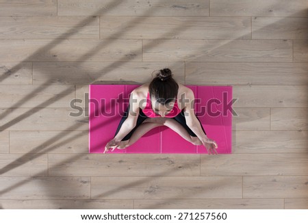 Top view, young woman meditating on a carpet in the lotus position, window casts graphics shadows on the wooden floor