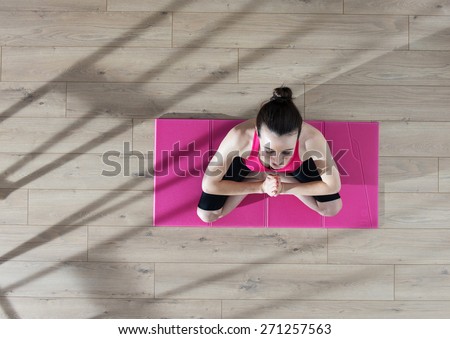 Top view, young woman meditating on a carpet in the lotus position, window casts graphics shadows on the wooden floor