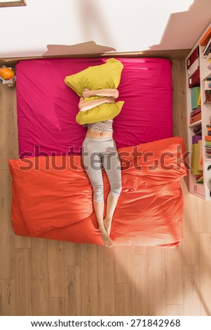 view from above anonymous young woman clutching a pillow in her bright colors bedding