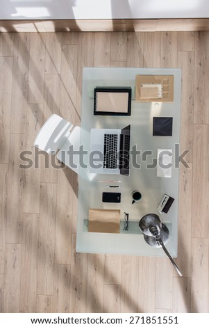 top view of a perfectly tidy glass desk with a laptop and a smartphone and other objects in the same color tone, sun casts graphics shadows  on the wooden floor