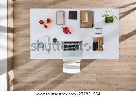 top view of a perfectly tidy white table with a laptop and a smartphone and other objects in the same color tone, sun casts graphics shadows  on the wooden floor