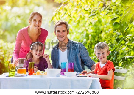 looking at camera, lovely family lunch in their garden on a sunny day, Mum is serving some apple juice, colors are bright