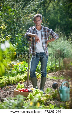 looking at camera, gardener standing in his garden, crate filled with vegetables at his feet