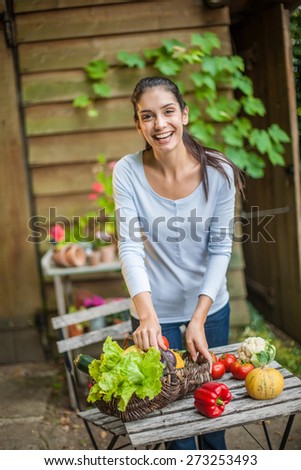 Smiling woman standing in front the garden table with a basket of fresh vegetables