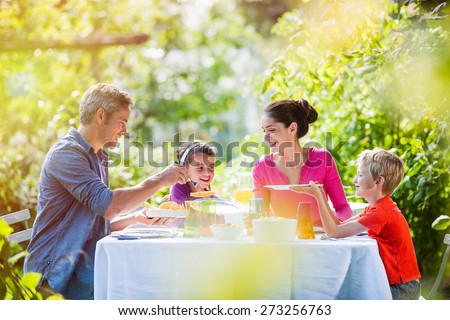 Summertime, nice family, Daddy, Mom and their two kids sitting at a table, eating lunch in the garden enjoying a sunny day