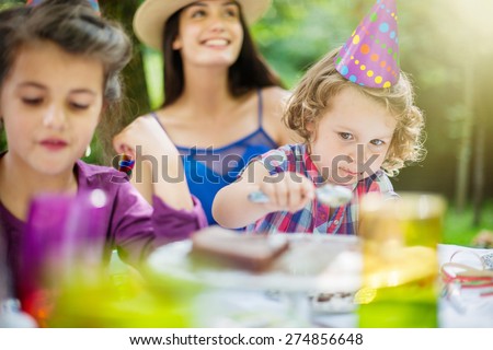Garden party, greedy little girl eating chocolate birthday cake in family