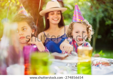 Garden party, greedy little girl eating chocolate birthday cake in family