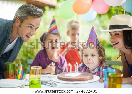 garden party with family for little girl\'s birthday, kid makes a wish and blows out the candles, the garden is decorated with balloons and colors are bright