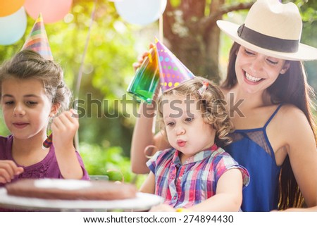 garden party with family for little girl\'s birthday, children blows out the candles on the cake, the garden is decorated with balloons and colors are bright