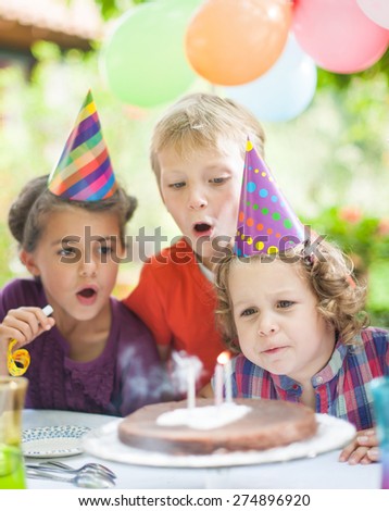 garden party with family for little girl\'s birthday, children blowing out the candles on the cake, the garden is decorated with balloons and colors are bright