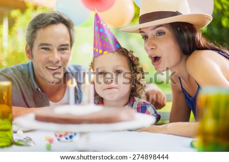 Garden party for daughter\'s birthday with mum and dad. Girl blowing her candles