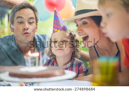 garden party for the little girl\'s birthday, the whole family helping her to blow out the candles, the garden is decorated with balloons and colors are bright