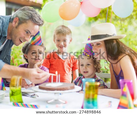 garden party with family for little girl\'s birthday, Dad lights the candles on the cake , the garden is decorated with balloons and colors are bright
